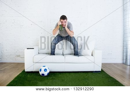 crazy football fan cheering watching television soccer match suffering stress nervous and excited jumping on sofa couch with ball and grass carpet emulating stadium pitch