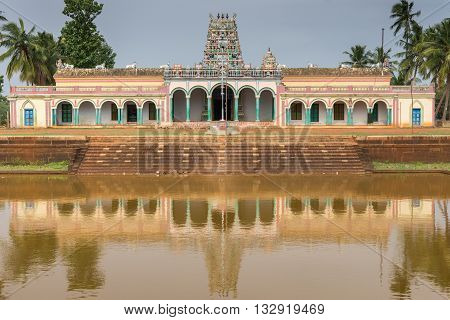 Chettinad India - October 17 2013: Closeup of Kothamangalam Shiva Temple reflected in temple pond filled with brown water. Vimanam tower in teh back. Green trees. All against blue sky.