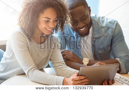 World of gadgets.  Smiling and positive modern young people sitting while using a digital tablet