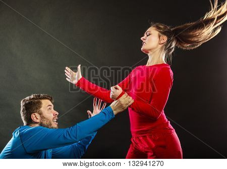 Wife abusing husband. Aggresive woman beating slapping scared man. Couple in studio on black. Domestic violence aggression. Bad relationship.