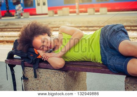 Beautiful female backpacker tourist napping on a bench and baggage at the station