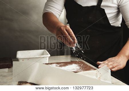 Man Pours Sugar Powder On Freshly Beked Chocolate Cakes In His Professional Artisan Confectionery