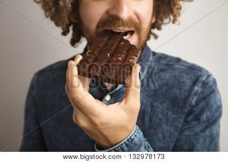 Close Focus On Hand,young Bearded Caucasian Man With Curly Hair Bites Bar Of Tasty Artisan Chocolate