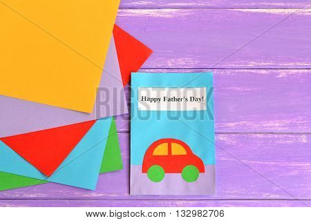 Greeting card with with paper car and text Happy father's day, pieces of colored paper on a light purple wooden background. Crafts card from colored paper. Gift idea for dad. Fathers day background.