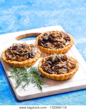 Homemade savory autumn tarts with fresh seasonal mushrooms in a crisp pastry base on blue background