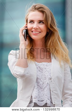 Young businesswoman talking on cellphone while walking outdoor. City business concept.
