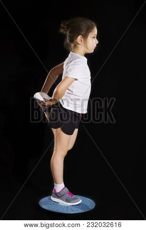 Little Caucasian Girl In On One Leg Position Staing On Balance Board. Photo On Black Background