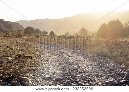 The Horizontal Shot Of Stone Dusty Road In A Dry Valley On A Background Of Bushes And Mountains. Ton