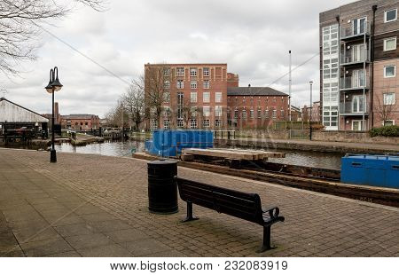 A Small Wooden Bench And Black Bin On The Towpath