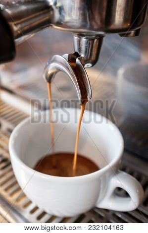 Fresh Espresso Dripping From Portafilter Of Coffee Machine Into White Cup