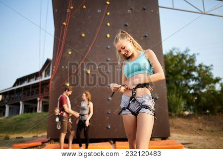 Pretty Caucasian Woman Puts On Belaying Harness For Practice On Artificial Rock Wall. Slim Strong He