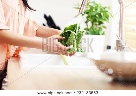 Young woman washing lettuce in modern kitchen