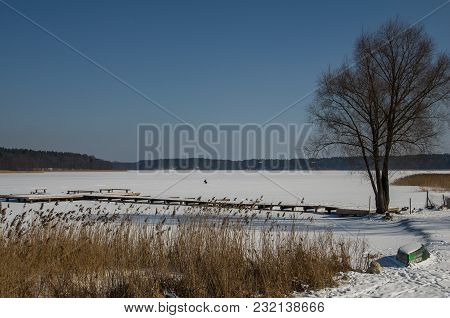 Winter Fishing On The Frozen Lake In The Sunshine Day. The Fisherman Is Fishing On The Ice Of The La