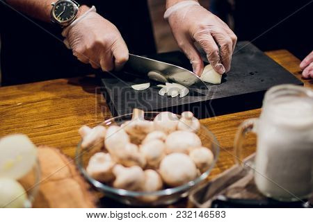 Chef's Hands With Knife Cutting The Onion On The Wooden Board. Preparation For Cooking. Healthy Eati