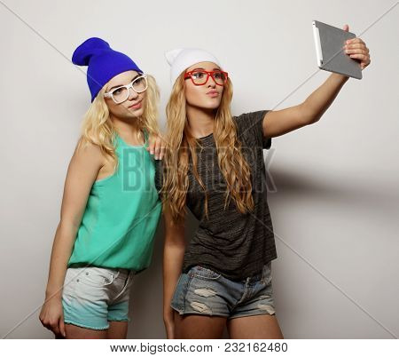 two hipster girls friends taking selfie with digital tablet, studio shot over gray vackground
