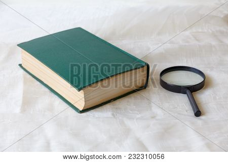 Old Book In Green Cover And A Magnifying Glass On A Light Background