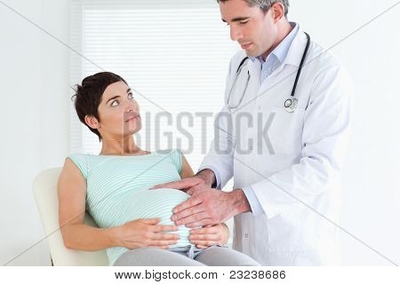 Auscultating 在一个房间里的怀孕妇女的肚子的医生