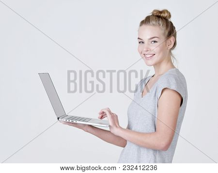 Young woman holds laptop in habds. Smiling caucasian girl with notebook posing at studio