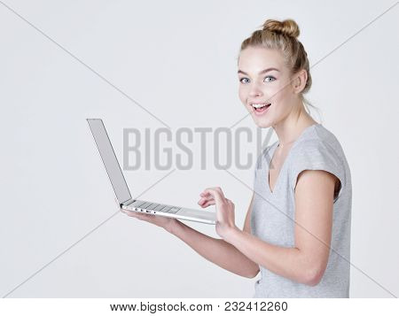 Young woman holds laptop in habds. Happy caucasian girl with notebook posing at studio