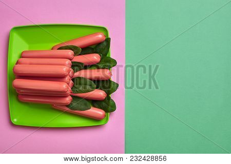 Sausages On A Plate With Spinach On A Green And Pink Minimal Background. Flat Lay. Top View. Still L