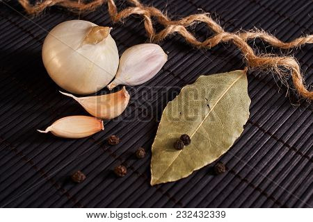 Onion, Garlic, Black Pepper And Bay Leaf On A Black Table