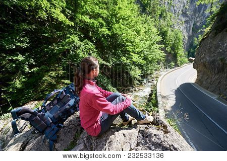 Girl Sitting On A Stone Beside A Backpack Under The Sunbeams Enjoying The Scenic Terrain Bicaz Canyo