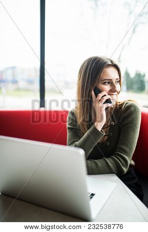 Happy Woman Using Laptop And Phone In Cafe. Young Beauty Girl Sitting In A Coffee Shop And Working O