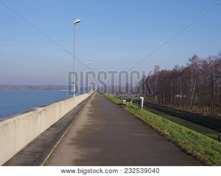 Walkway With Lamps On Barrage At Countryside Landscapes Of Green Grassy Field, Forest On Artificial 