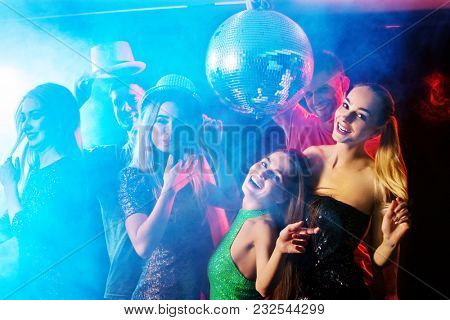 Dance party with group people dancing. Women and men have fun in night club. Rest after hard day at work. Back light on girls hair. People in brilliant suits dance under influence of alcohol.