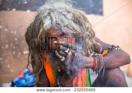 VARANASI, INDIA - MAR 16, 2018: Hindu sadhu smoking ganja, marihuana with chillum  on the ghats of the Ganges river. According to legends, the city was founded by God Shiva about 5000 years ago.