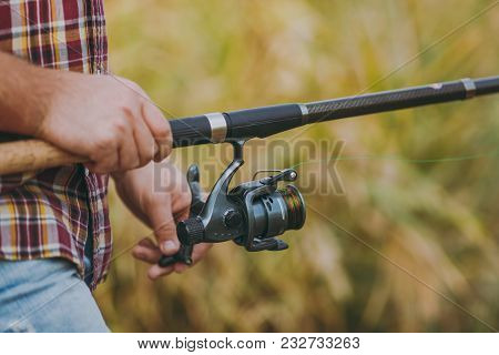 Close Up A Man Holds And Untwists A Fishing Reel In His Hands On A Blurry Brown Background. Lifestyl
