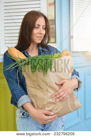 A Smiling Girl In A Jeans Jacket Is Holding A Paper Bag With Food In Her Hands. The Woman Stinted In