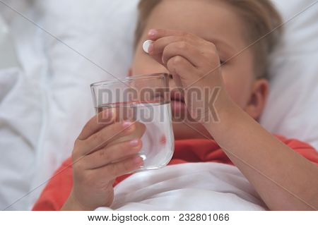 Close-up - Little Sick Cute Cboy Holding A Pill And A Glass Of Water Lying On The Bed