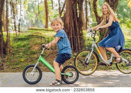 Happy Family Is Riding Bikes Outdoors And Smiling. Mom On A Bike And Son On A Balancebike.