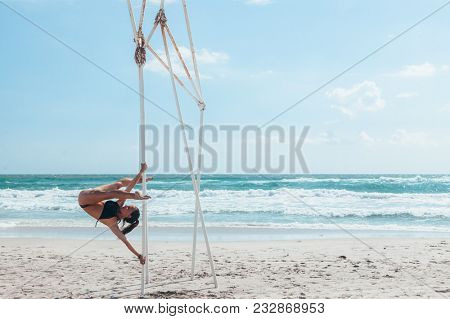 Pole dance outdoors. Young slim girl doing poledance on the beach over sea.