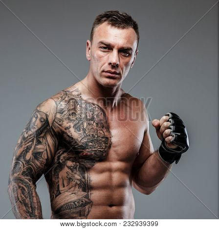 Muscular Tattooed Fighter Against Grey Background. Studio Shot