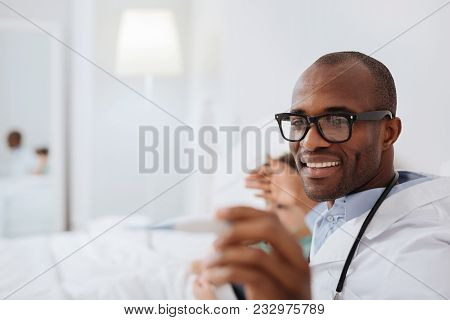 Right Thermoregulation. Skillful Satisfied Male Doctor Touching Boys Forehead While Smiling And Carr