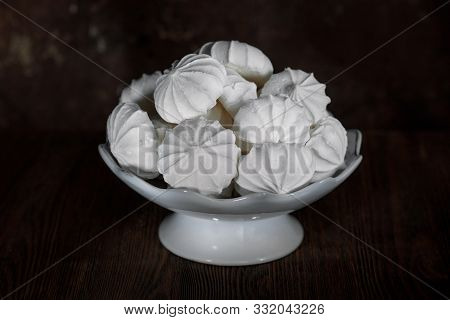 White Meringues In A White Porcelain Vase On A Dark Brown Background