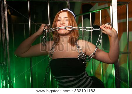 Sweet Plus Size Woman In A Carnival Striped Inmate Costume Stands Near The Prison Cage And Is Sad In