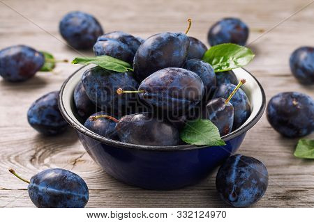 Full Bowl Of Freshly Harvested Ripe Prune Fruits On Wooden Table Closeup