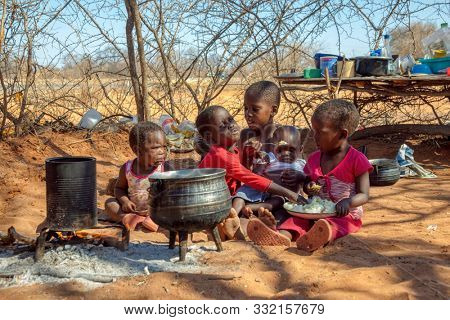 two african children in a village near Kalahari desert, the sister feeding her brother in the outdoors kitchen