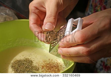 The Girl Rubs A Nutmeg On A Fine Grater In A Bowl With Dough. The Process Of Making Cream Sauce With