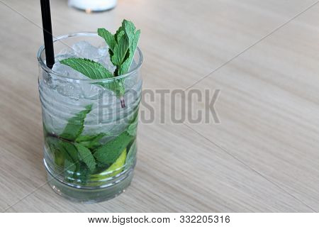 Glass Of Mochito Cocktail On Wooden Table With Black Straw, Ice And Mint Leaf. Copy Space For Text. 
