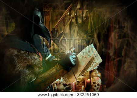 The plague doctor is working at his desk, inventing a cure for bubonic plague. The atmosphere of mysticism. Historical reenactment. Halloween. 