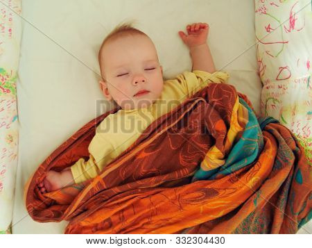 The Little Baby Sleeps Sweetly In His Crib In A Plaid, In A Sling, In A Blanket. The Baby Girl Sleep