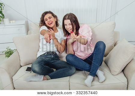 Joyful Girlfriends Are Laughing Desparately, Pointing Their Fingers At The Camera, Sitting On The So