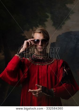 Handsome Man In A Royal Red Doublet And Sunglasses. Funny Duet Of Medieval Style And Modern Attribut