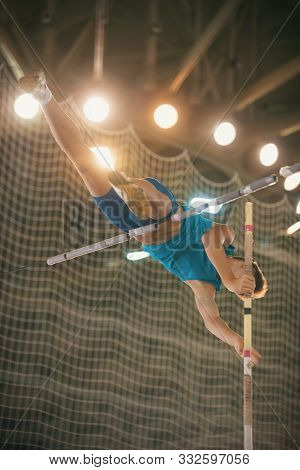 Pole Vaulting - Guy In Blue T Shirt Is Jumping Over The Bar Holding On To A Pole