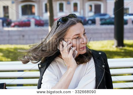 Cheerful Beautiful European Female In Her Fifty Enjoying The Nice Summer Weather Outdoors, Sitting O