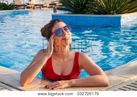 Portrait Of Happy Young Woman In Sunglasses And Red Swimsuit In Swimming Pool.
